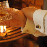 Cufflinks by a fireplace with a glass of whisky. Showing bronze cufflinks with a blue patina.