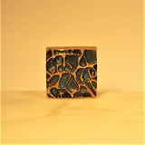 Square bronze sculptural cufflink on white marble base